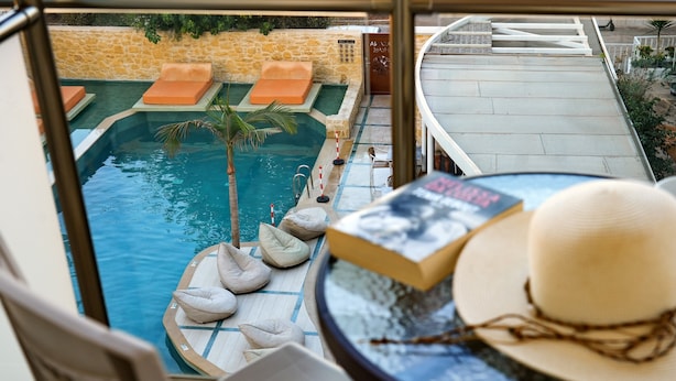 Vista de la piscina con sillones de descanso, una palmera y un libro sobre una mesa.