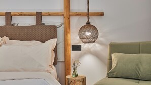 Un dormitorio con cama, sofá verde, cabecero de madera, lámpara colgante y un taburete de madera con un florero.
