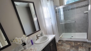 A modern bathroom with two sinks, a large mirror, a shower with a glass door, and a stone tile floor. - Hillside Relaxation in Endless Mountains. Minutes from Tioga Downs. Sleeps 8 (Rome)