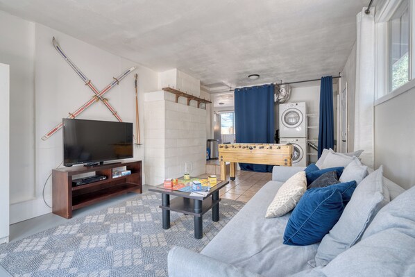 Una sala de estar con un sofá, una mesa de centro con juegos de mesa, una televisión y una mesa de fútbol.