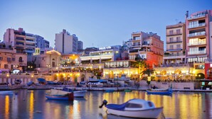 A waterfront area with boats docked, buildings with shops, and a prominent Dolce Vita sign. - Contemporary 3BR Retreat in Prime Sliema (Sliema)