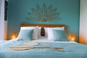 Ein ordentlich bezogenes Bett mit blauer Tagesdecke, zwei Kissen und einer Wanddekoration.