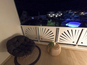 Un balcone con vista su una piscina e case di notte. Sul pavimento, due sacchi di fagioli e un cesto di vimini.