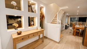 A modern interior with a wooden console table, a staircase, and a dining area.