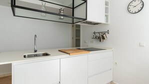 Una cucina moderna con lavello in acciaio inossidabile, piano di lavoro in legno, mobili bianchi, un vaso di vetro e una sveglia a parete.