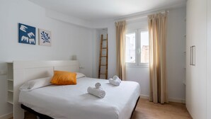 Camera d'albergo con un letto, biancheria da letto bianca, un cuscino arancione, una scala in legno e due asciugamani arrotolati.