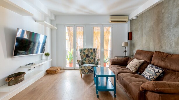 Un soggiorno con un divano in pelle marrone, un tavolino da caffè blu, una TV a parete e un balcone con vista.
