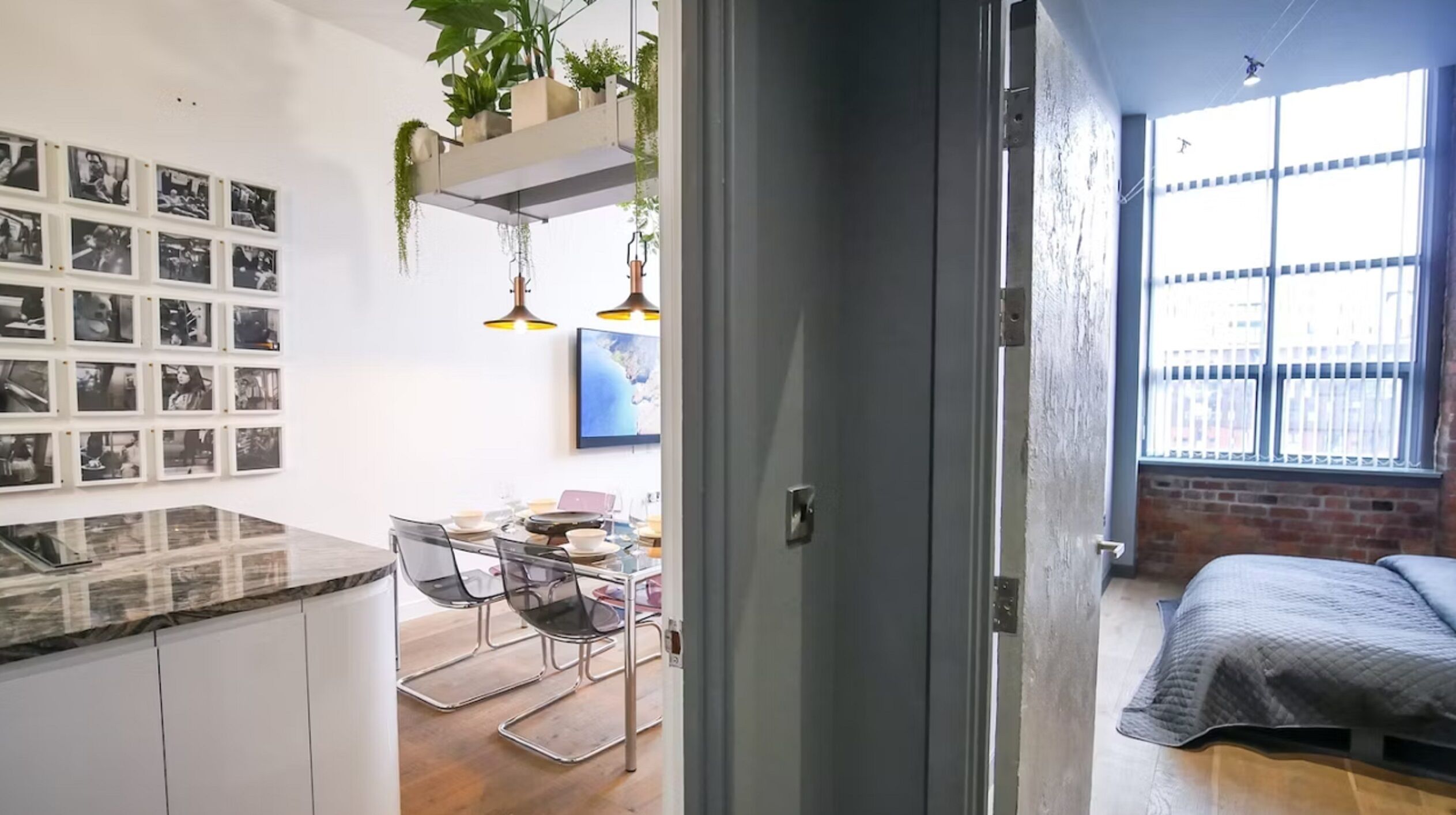 Une cuisine moderne dotée d’un plan de travail en marbre, un coin repas avec une table et des chaises, et une chambre avec un lit et une grande fenêtre.