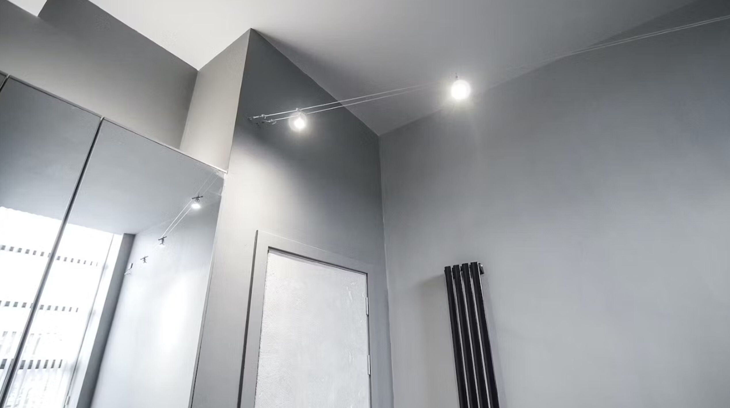 Et moderne badeværelse med et stort spejl, indbyggede loftslamper, en radiator og en dør.