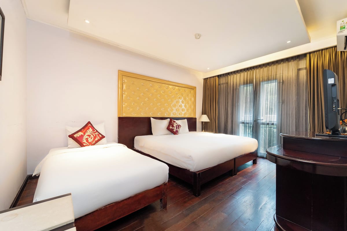 A hotel room with two beds, a wooden headboard, a desk, and a large window with curtains.