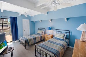Camera da letto con due letti, ventilatore a soffitto, televisione e balcone con vista.