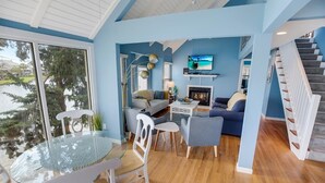 Uma sala de estar moderna com uma mesa de vidro, cadeiras brancas, um sofá azul e uma lareira.