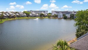 Vista para o lago de uma área residencial com vários edifícios de apartamentos, uma fonte e vegetação exuberante.