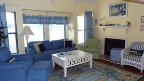 A living room with a blue sofa, a white coffee table, a green armchair, a striped armchair, a fireplace, and a colorful rug.