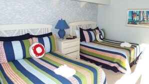 A bedroom with two beds, striped bedding, a nightstand with a lamp, and a wall painting.