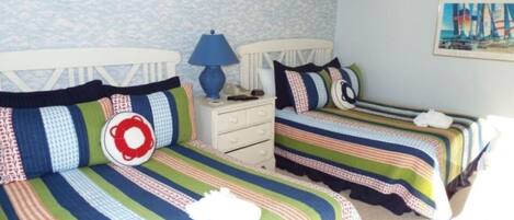 Een slaapkamer met twee bedden, gestreept beddengoed, een nachtkastje met een lamp en een schilderij aan de muur.
