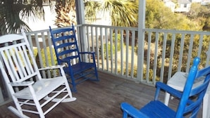 A wooden deck with two rocking chairs and a table, surrounded by a white railing.