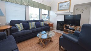 Una sala de estar con sofá, sillones, una mesa de centro de vidrio, chimenea y televisor.