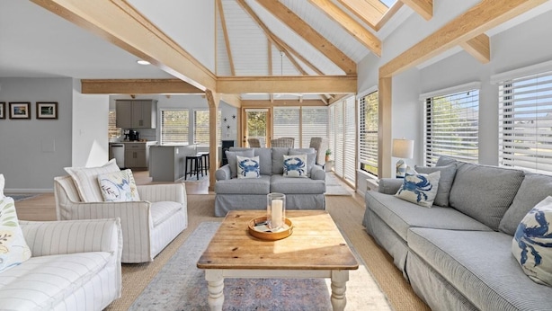 A spacious living area with a high ceiling, wooden beams, and large windows.
