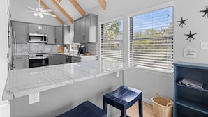 A modern kitchen with a marble countertop, grey cabinets, a microwave, and a ceiling fan.