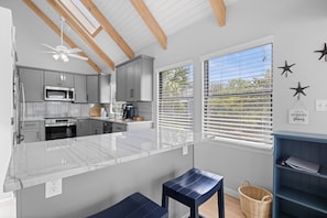 A modern kitchen with a marble countertop, grey cabinets, a microwave, and a ceiling fan.