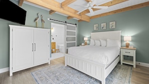 A bedroom with a bed, white wardrobe, ceiling fan, and artwork on the wall.