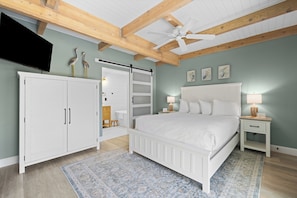 A bedroom with a bed, white wardrobe, ceiling fan, and artwork on the wall.