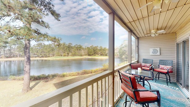 Une véranda couverte offre une vue sur un lac et des arbres. On y trouve une table avec des chaises et un banc.