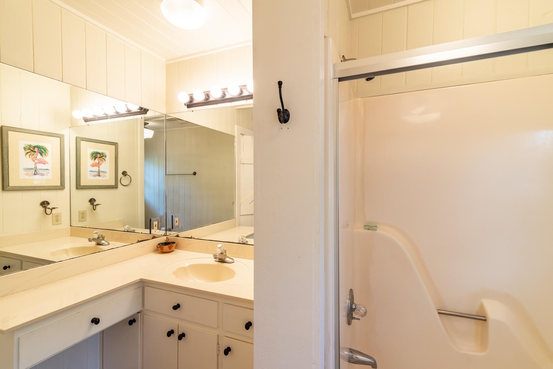 A bathroom with a large mirror, two sinks, a shower, and a door leading to another room.