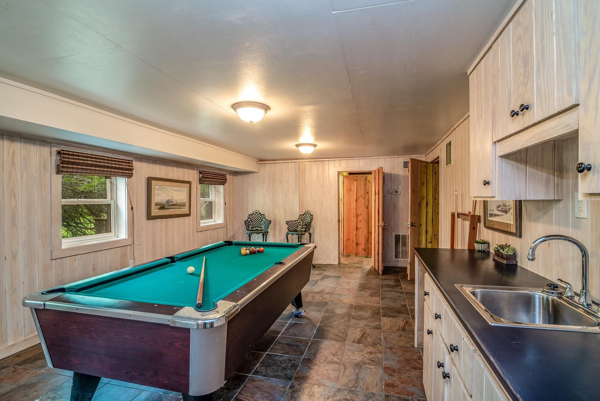 A pool table in a room with wooden walls and a kitchen area.