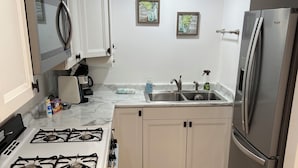 A compact kitchen with white cabinets, a stainless steel refrigerator, a gas stove, and a wooden countertop.