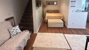 A modern living room with a sofa, a bed, a staircase, and a kitchen area.