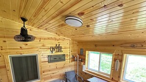 A cabin interior with a sofa, a table, a chair, a ceiling fan, and a staircase.