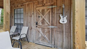 Une porte en bois avec une guitare accrochée, deux chaises à l’extérieur et une fenêtre avec des stores.