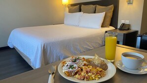 A hotel room with a neatly made bed, a breakfast table with a plate of food, a glass of orange juice, and a cup of coffee. - ALTAVISTA (Reynosa)