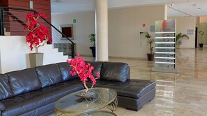 A spacious lobby with a leather sofa, a glass coffee table, and a staircase with red flowers. - ALTAVISTA (Reynosa)