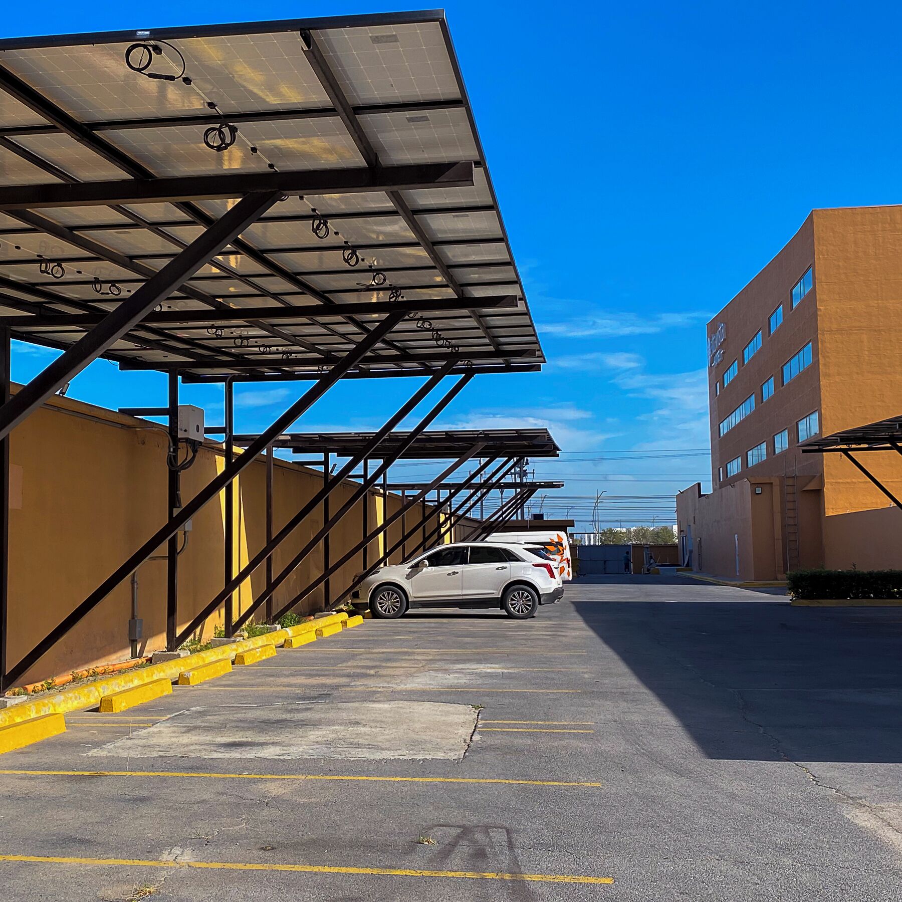 A parking garage with a covered walkway and a white car parked in the lot.