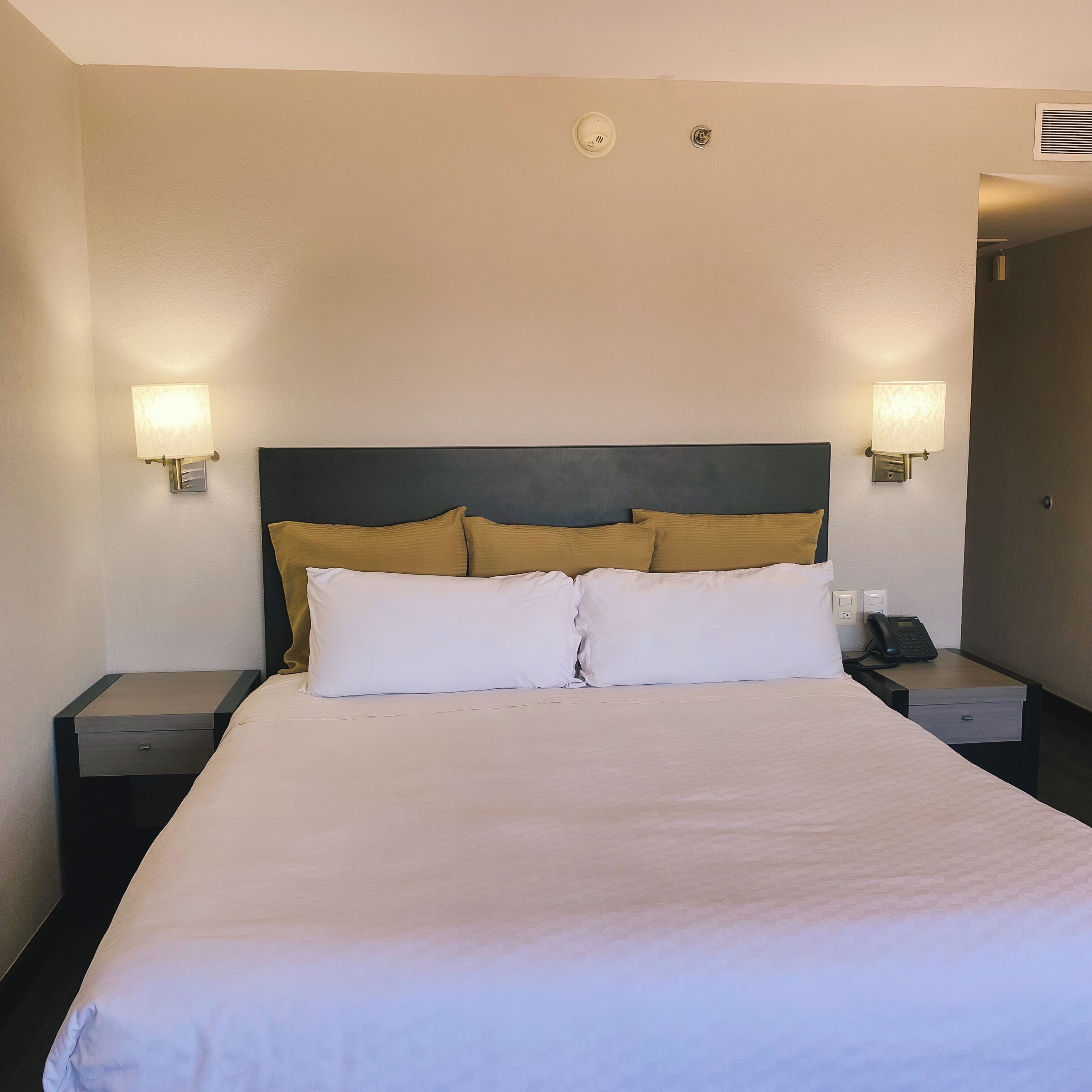 Habitación de hotel con una cama grande, dos mesitas de noche, un teléfono y dos lámparas de pared.