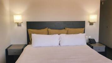 Habitación de hotel con una cama grande, dos mesitas de noche, un teléfono y dos lámparas de pared.