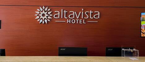 Mostrador de recepción en el Hotel Altavista, con un logo, el nombre del hotel y dos monitores de computadora negros.