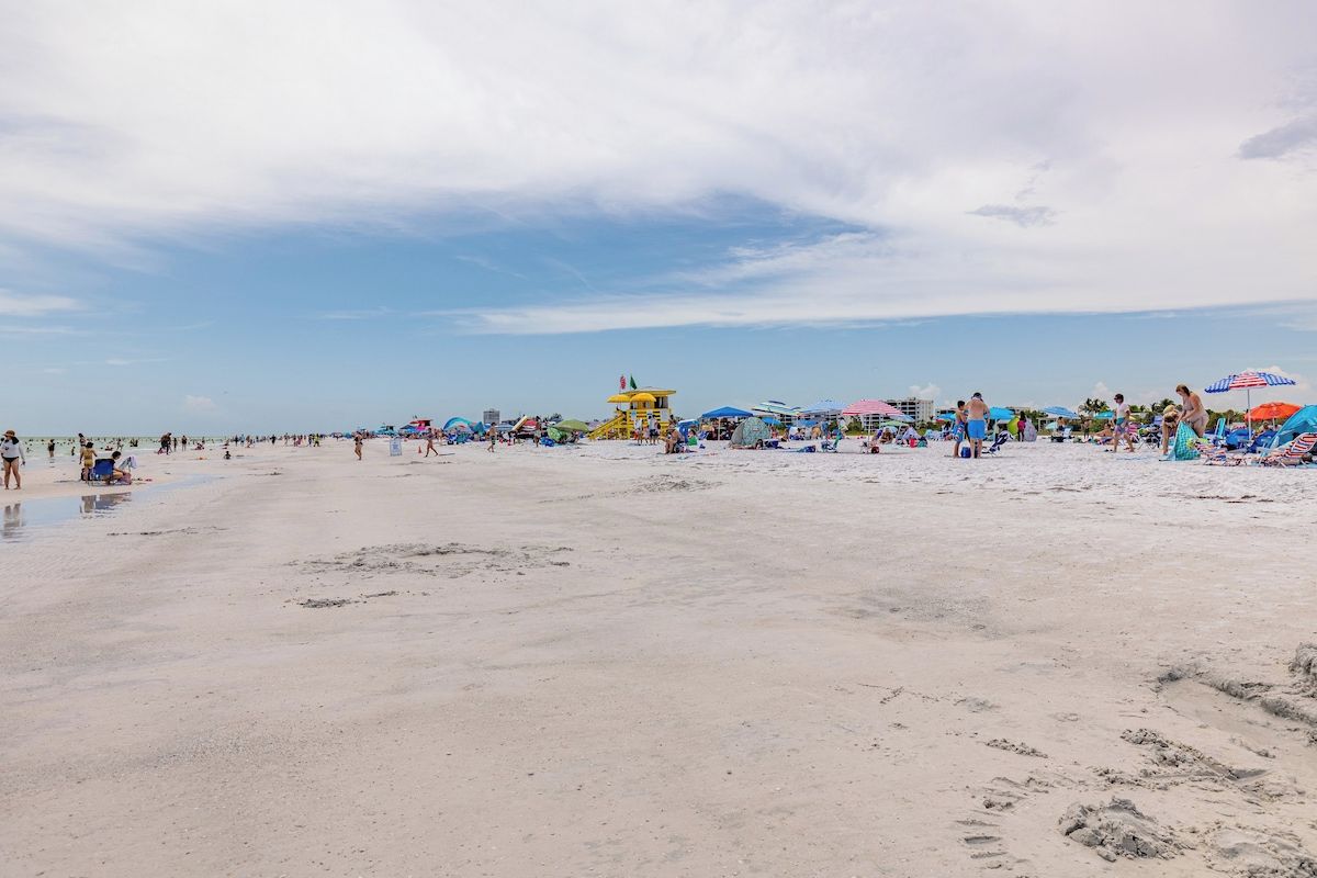 A beach with umbrellas and beach chairs, a lifeguard tower, and people enjoying the beach.