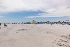 A beach with umbrellas and beach chairs, a lifeguard tower, and people enjoying the beach.