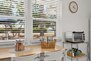 A kitchen with a wooden table, white chairs, a toaster, and a window with blinds.