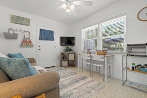 A compact living space with a sofa, a dining area, a television, and a window with blinds.