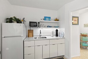 A kitchen with white cabinets, a microwave, a sink, and a refrigerator.