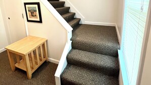 Una escalera con peldaños alfombrados, barandilla de madera y una pequeña mesa al pie.
