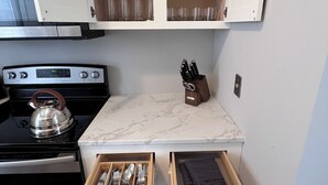 A compact kitchen with a stove, kettle, and drawer with utensils. - Spacious 3 Bedroom Sleeps 5 - Walk to Botanical Garden - Long Term Pet Friendly (St. Louis)