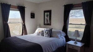 A bedroom with a bed, a bedside table with a lamp, and a window with curtains.