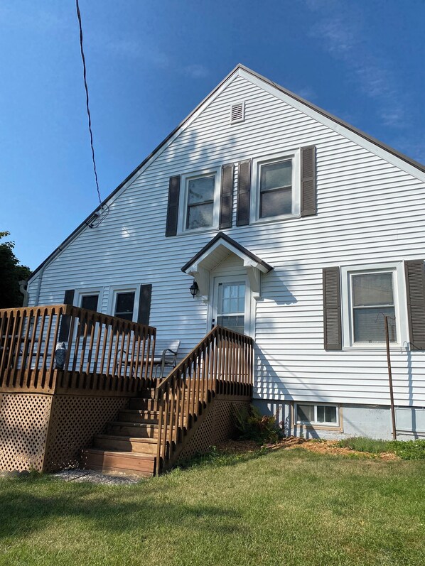 A two-story house with a front porch, a wooden staircase, and a fenced yard.