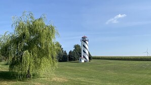 A lighthouse with a striped pattern, a weeping willow tree, and a wind turbine in the background.